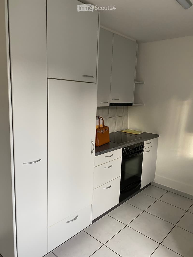 Modern kitchen with white cabinets, tiled floor, induction cooktop, oven, and a handbag on the counter.