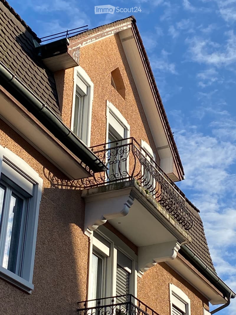 Multi-story building with beige textured walls, white-framed windows, and ornate metal balconies.