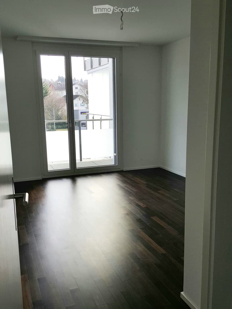 Empty room with wooden flooring and large sliding glass doors leading to a balcony or outdoor area.