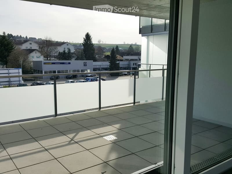 Balcony with tiled floor, metal railing, and a view of a parking lot and surrounding buildings.