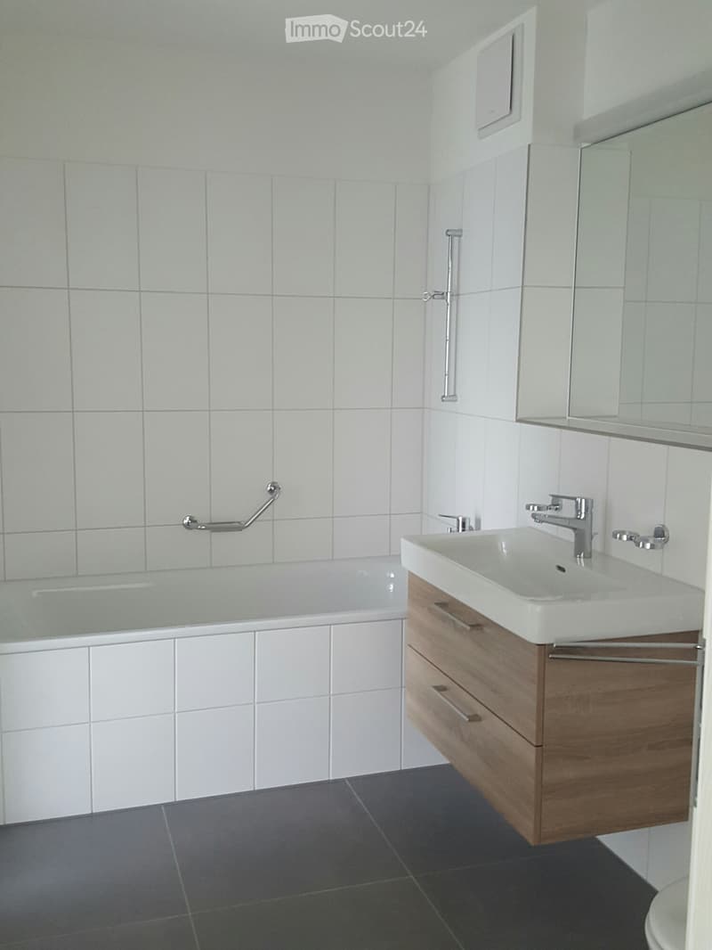 Modern bathroom with white tiled walls, a bathtub, a sink with a wooden cabinet, and a mirror above the sink.