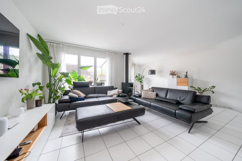 Modern L-shaped black leather sofas, central wooden coffee table, white tiled floor, potted plants, television