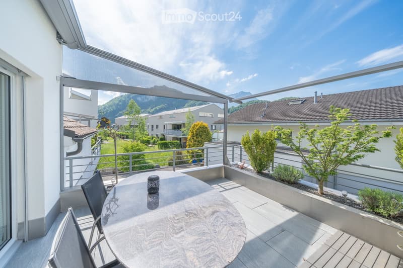 Terrace with round table and chairs, metal railing, outdoor lighting, and mountain view.