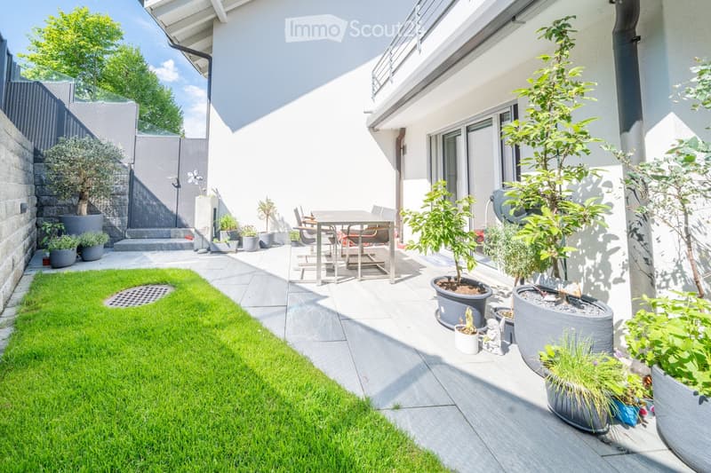A garden with a patio, dining table, potted plants, and grass.