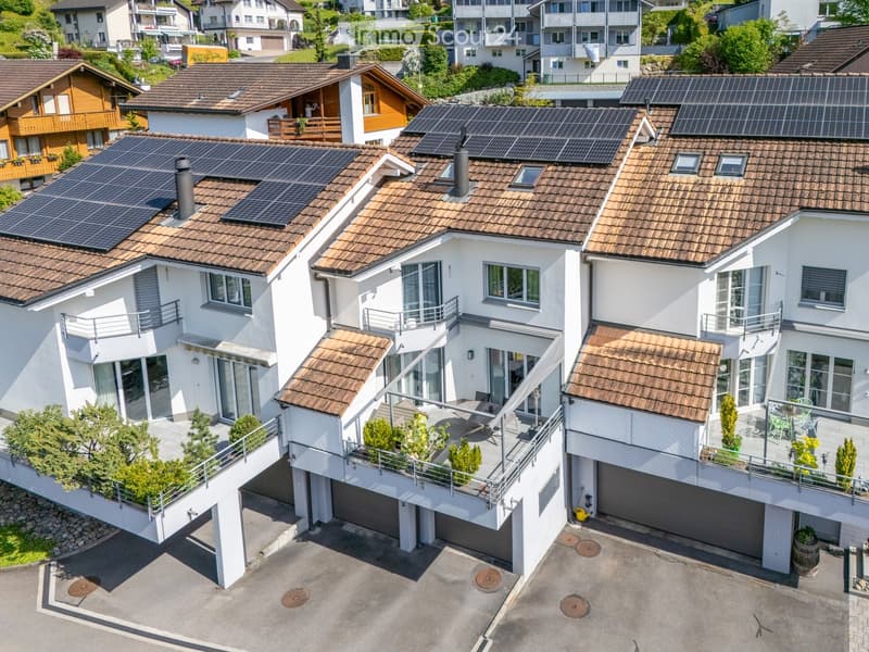 A row of modern houses with solar panels on the roofs, multiple balconies, and a parking area in front.