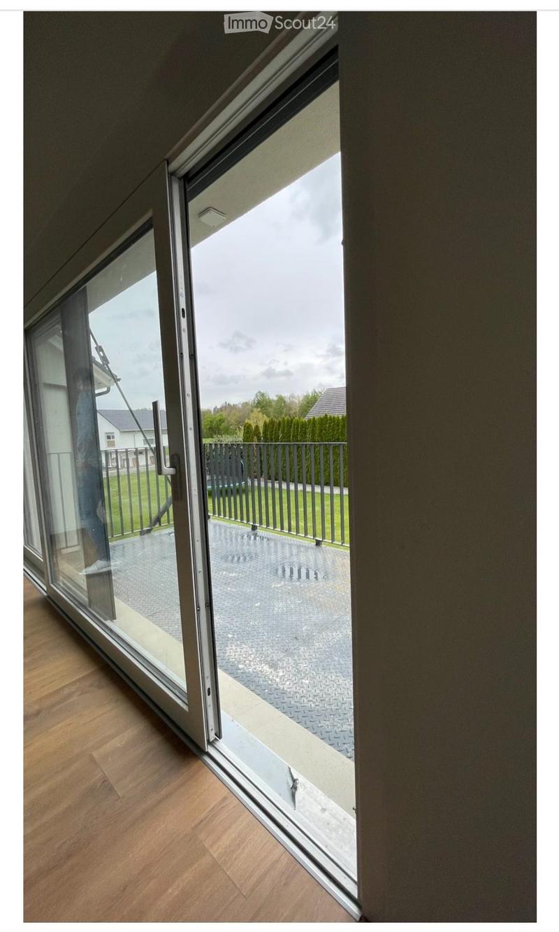 Large sliding glass door opening to a balcony with a metal railing, wooden floor inside, and a paved outdoor area.