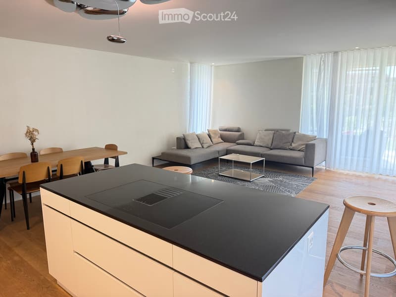 Modern open-plan living and dining area with a grey sectional sofa, coffee table, dining table with chairs, and a kitchen island with a black countertop.