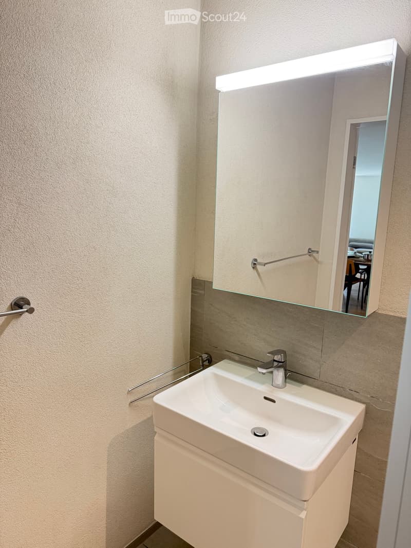 Modern bathroom with a white sink, chrome faucet, built-in mirror with built-in lighting, and towel rack.