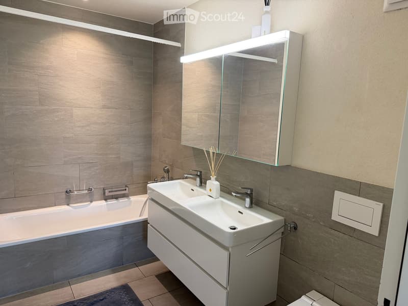 Modern bathroom with a bathtub, double sink, mirrored cabinet, and sleek fixtures.
