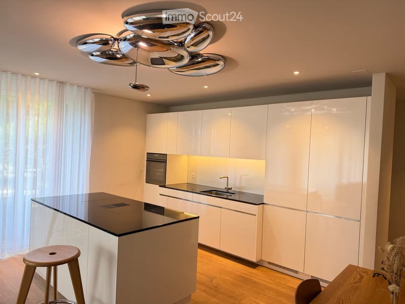 Modern kitchen with white cabinets, black countertop, stainless steel sink, and a sleek chandelier.