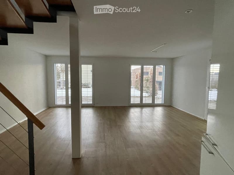 Empty room with wooden flooring, large windows, and a staircase leading upwards.
