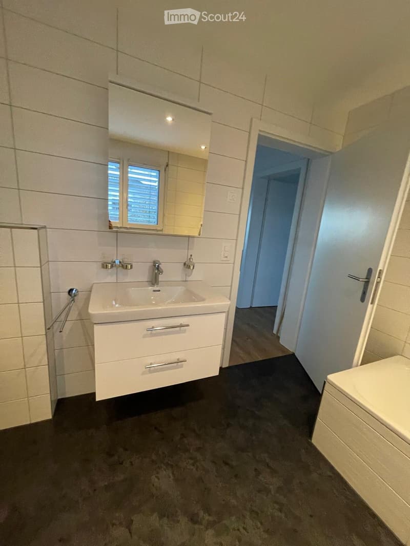 Modern bathroom with a white sink, mirror, and cabinet. The room features tiled walls and a dark grey carpeted floor.