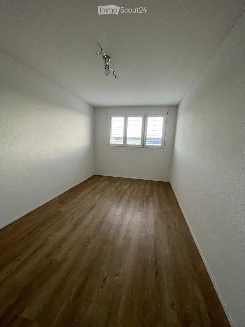Empty room with wooden flooring, white walls, and a window with blinds.