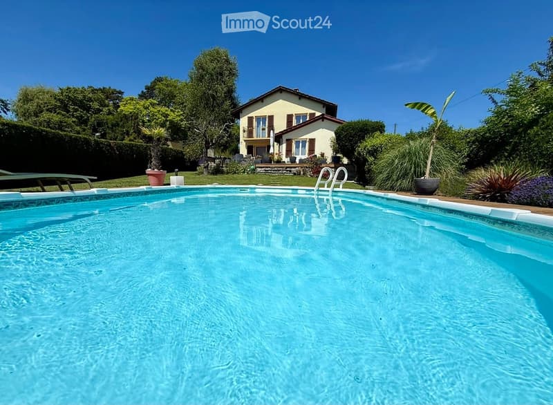 A private swimming pool in a well-maintained garden area with a house in the background, surrounded by greenery and potted plants.