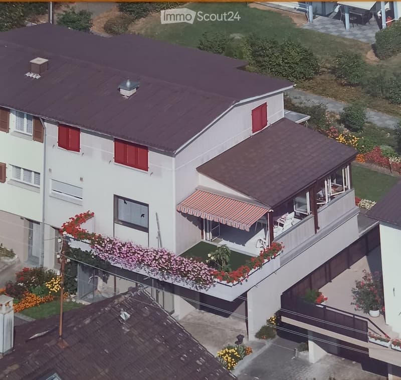 Two-story house with red shutters, a balcony with flower boxes, and a covered patio area with outdoor furniture.