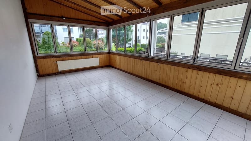 Empty sunroom with wooden paneling, tiled floor, large windows, and radiator along one wall.