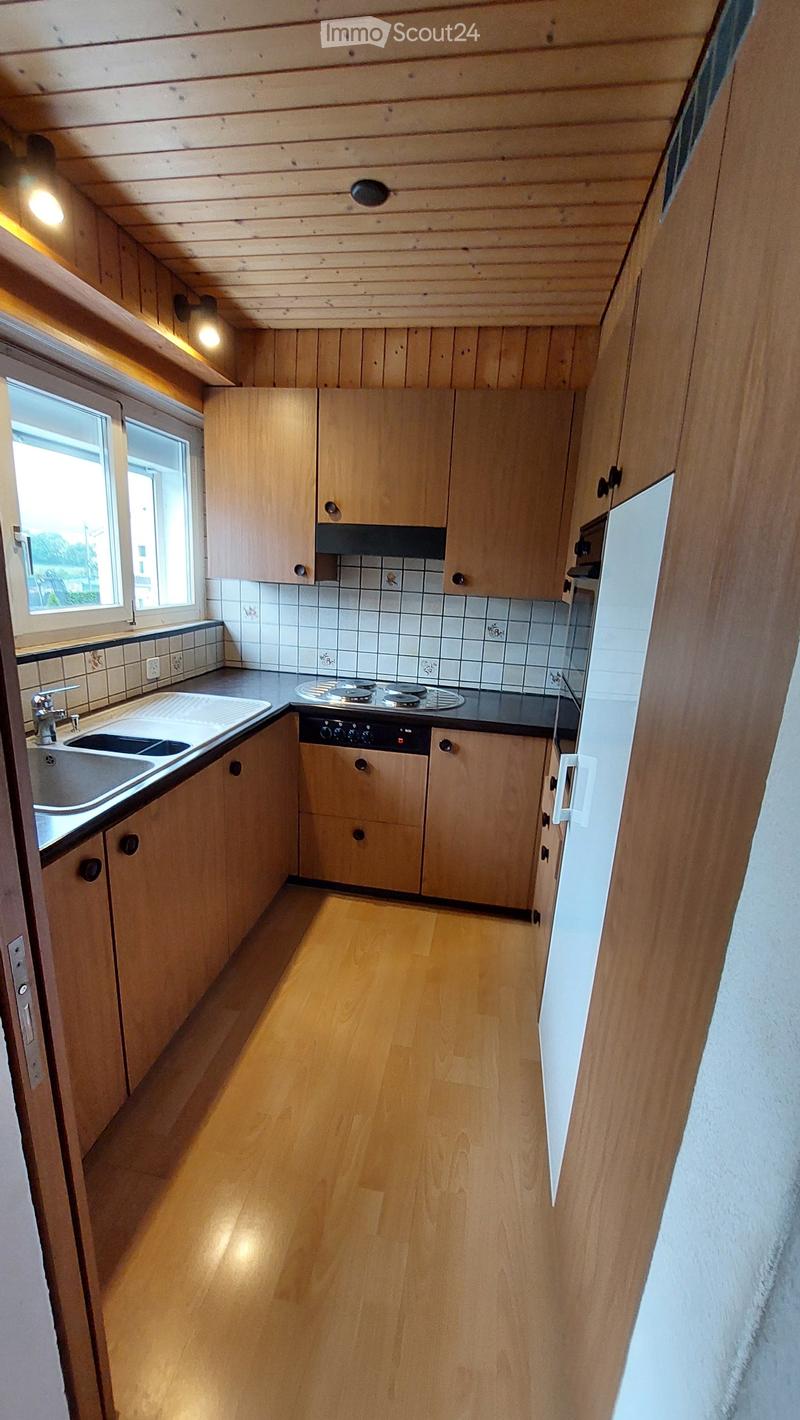 Bright kitchen with wooden cabinets, a sink, a stove, and a dishwasher. The floor is wooden, and the walls are tiled in the backsplash area.