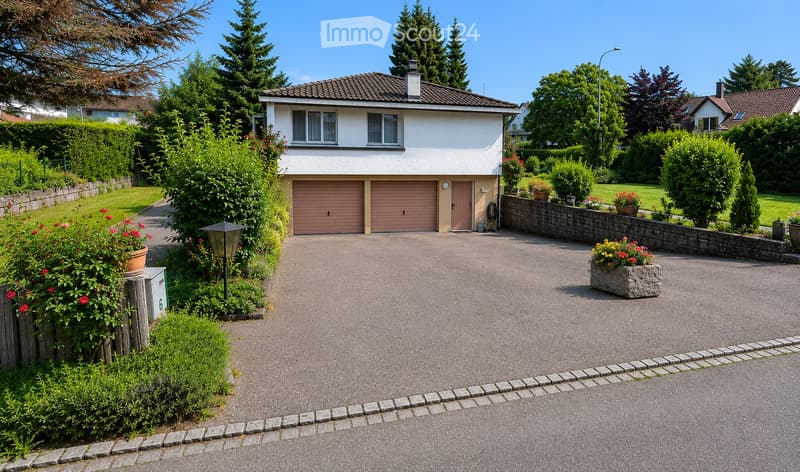 Two-story house with a garage, surrounded by greenery and a well-maintained driveway.