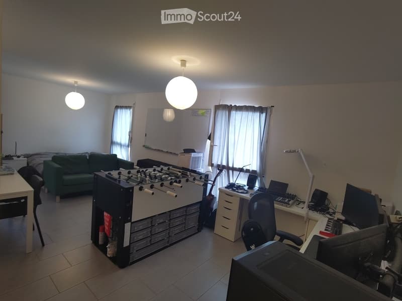 A multi-purpose room with a green sofa, a foosball table, a desk with a laptop, and a futon with a mattress and pillows.
