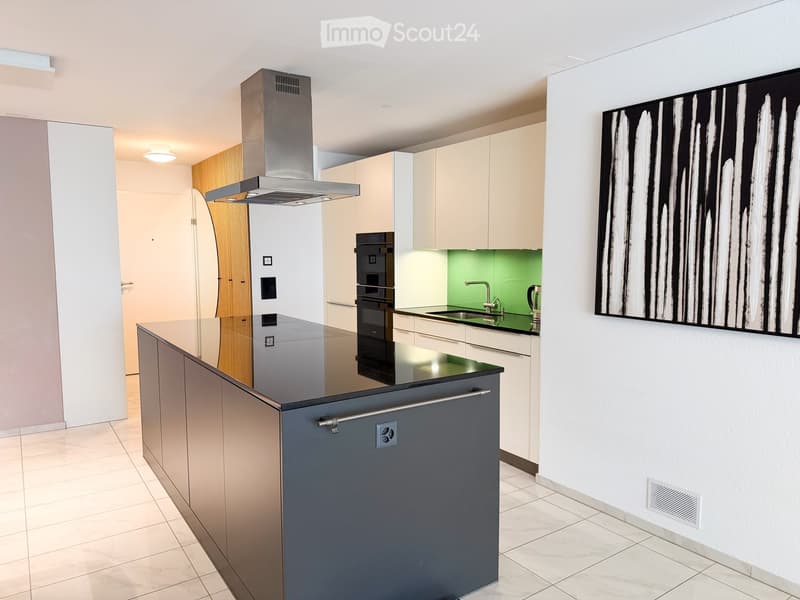 Modern kitchen with light-colored cabinets, a central island, stainless steel appliances, and a sleek black countertop.