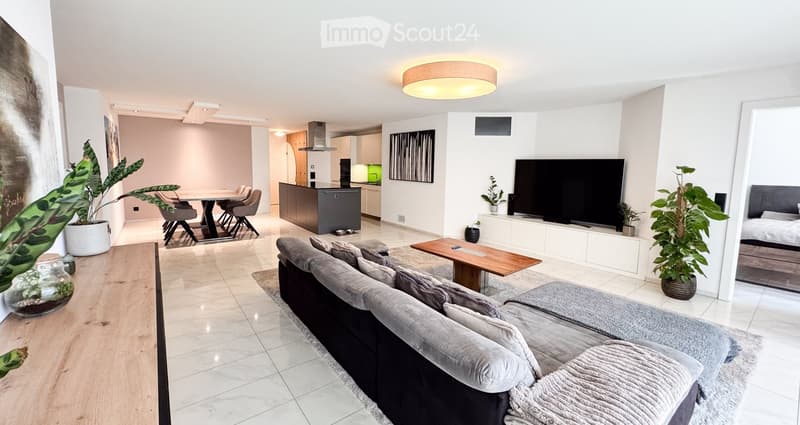 Modern, open-concept living and dining area with a grey sectional sofa, wooden coffee table, flat-screen TV, dining table with chairs, and a kitchen island.