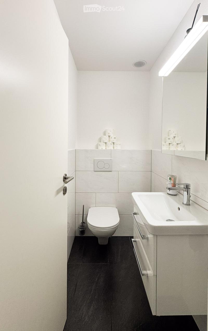 Modern bathroom with white tiles, black floor, toilet, sink, mirror, and toilet paper on shelves.