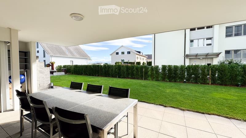 Outdoor dining area with a table and chairs, overlooking a well-maintained lawn and surrounding houses.