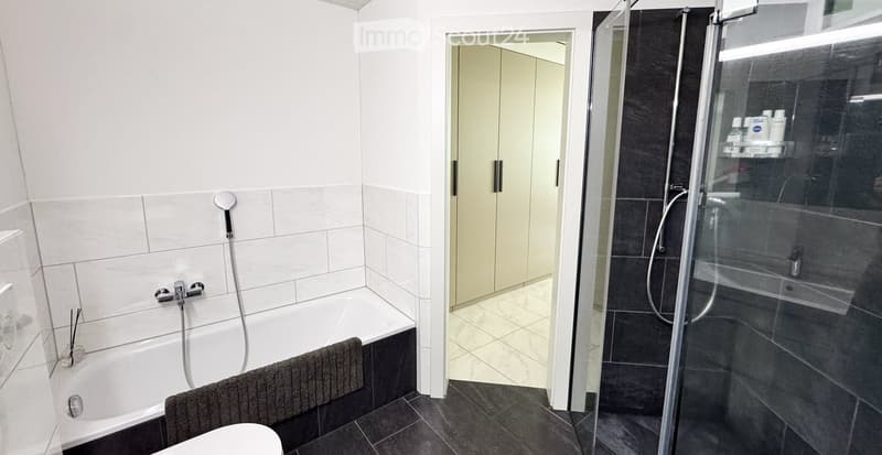 Modern bathroom with a white bathtub, glass-enclosed shower, and built-in white cabinets.