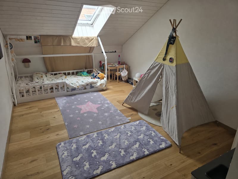 Cozy children's bedroom with wooden floors, bunk bed, desk, toy tent, and colorful rugs.