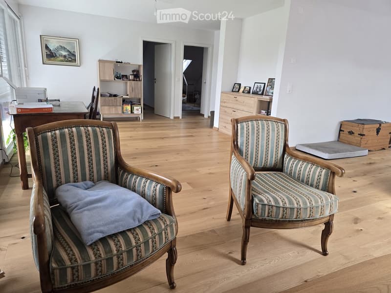 Spacious living room with wooden flooring, two armchairs with striped upholstery, a small table, a cabinet, and a printer on a desk.
