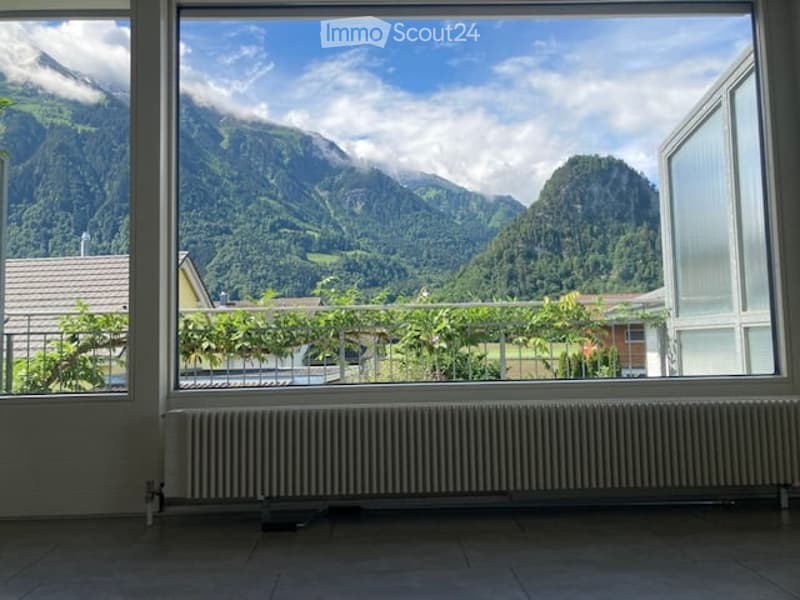 Empty room with large windows offering a scenic mountain view, radiator below the windows, and a metal railing outside.
