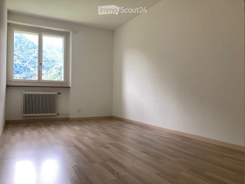 Empty room with wooden flooring, white walls, and a single window with a radiator below it.