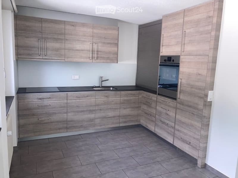 Modern kitchen with light wood cabinets, black countertops, and stainless steel sink and oven.