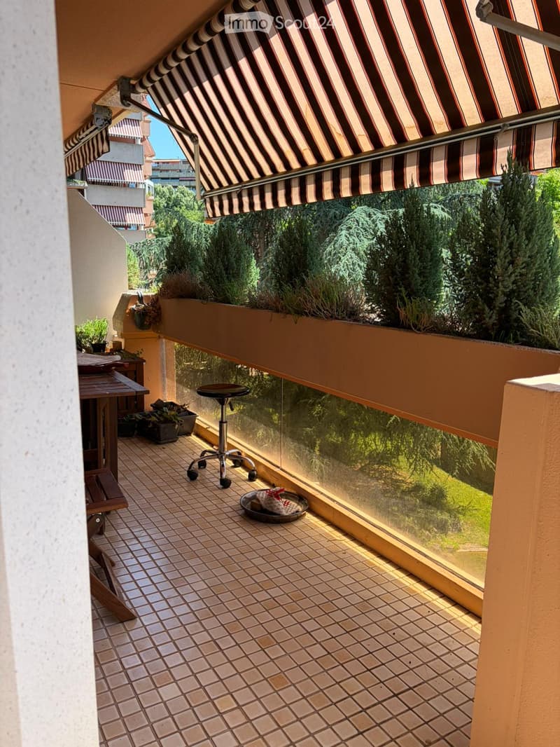 Balcony with tiled floor, glass railing, and outdoor furniture including a stool, table, bench, and potted plants.