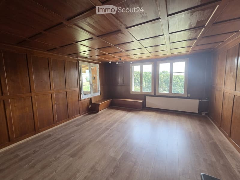 Empty room with wooden walls, wooden floor, large windows, and built-in benches along one wall.