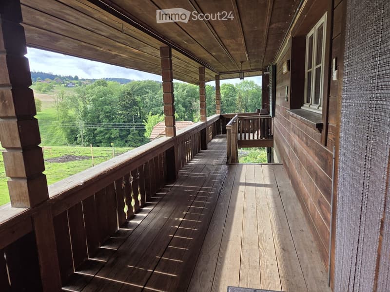 Wooden balcony with railings, wooden floor, and scenic countryside view.
