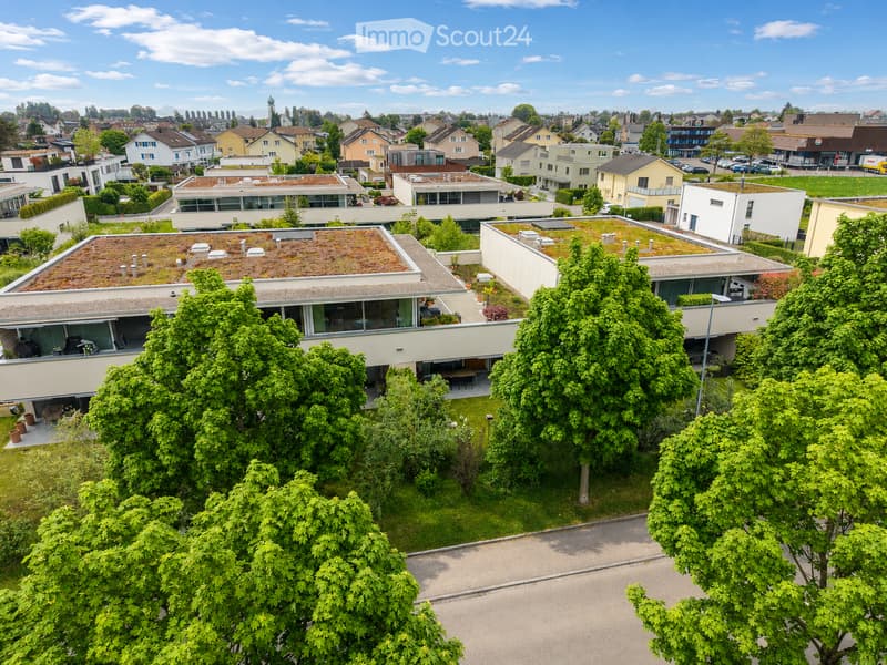 Aerial view of a modern residential complex with multiple buildings, green roofs, and surrounding greenery.