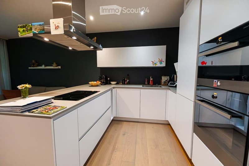 Modern kitchen with white cabinets, induction stove, built-in oven, and a sleek design. Includes a vase with flowers, a bowl on the counter, and decorative items on shelves.
