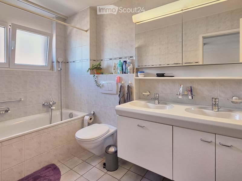 Bathroom with bathtub, toilet, double sink, and a window