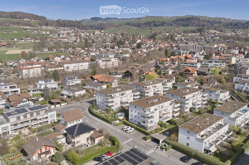 Aerial view of a town with many buildings, some with solar panels, surrounded by green fields and hills.