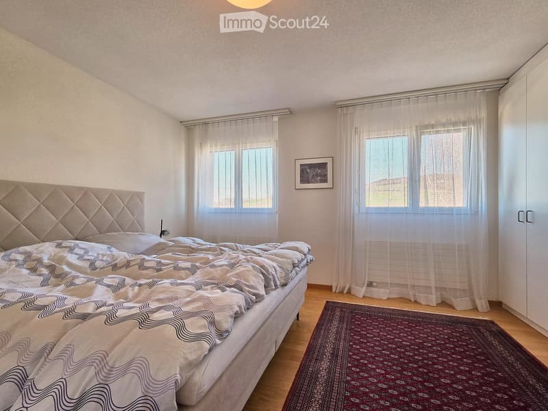 Bedroom with bed, two windows, white walls, wooden floor, rug, picture frame, wardrobe