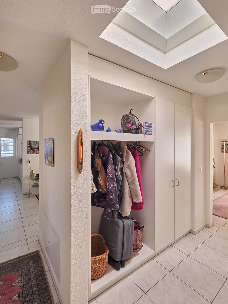 A hallway with a white wardrobe, a shelf with clothes, a basket, and a rug.