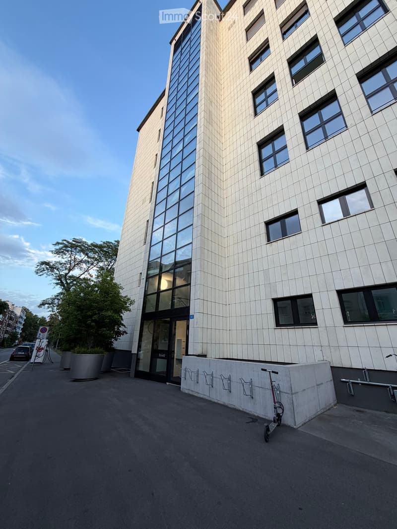 Modern multi-story building with a combination of glass and tiled facade, featuring large windows and a sleek entrance.
