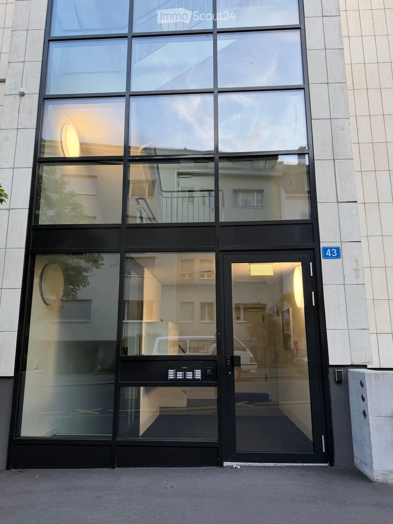 Modern building entrance with large glass windows and doors, featuring a black door frame and a blue sign displaying the number 43.