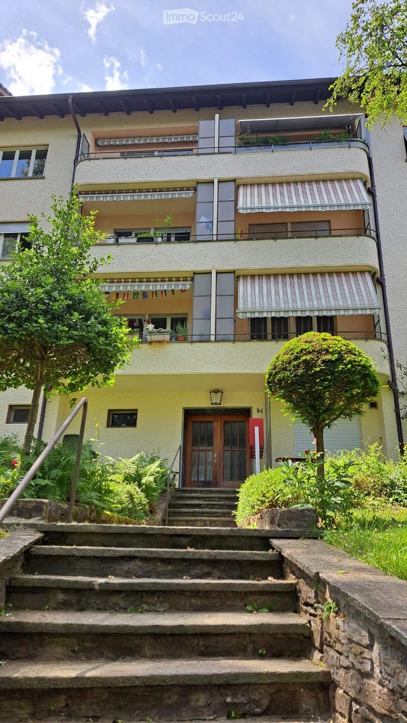 A multi-story residential building with balconies, striped awnings, and a staircase leading to the entrance.