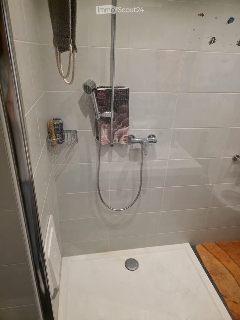 Modern bathroom with a bathtub, showerhead, and faucet. Includes a towel hanging on the wall and a small shelf with toiletries.