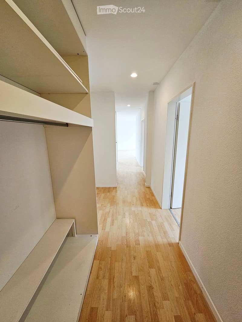 Empty hallway with wooden flooring, white walls, and built-in shelving on one side.