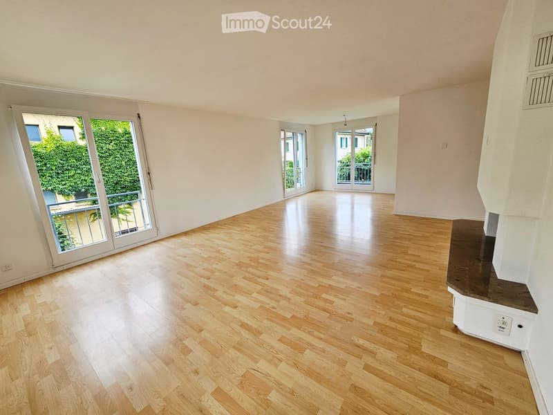 Empty room with light wooden flooring, white walls, large windows, and sliding doors leading to a balcony.