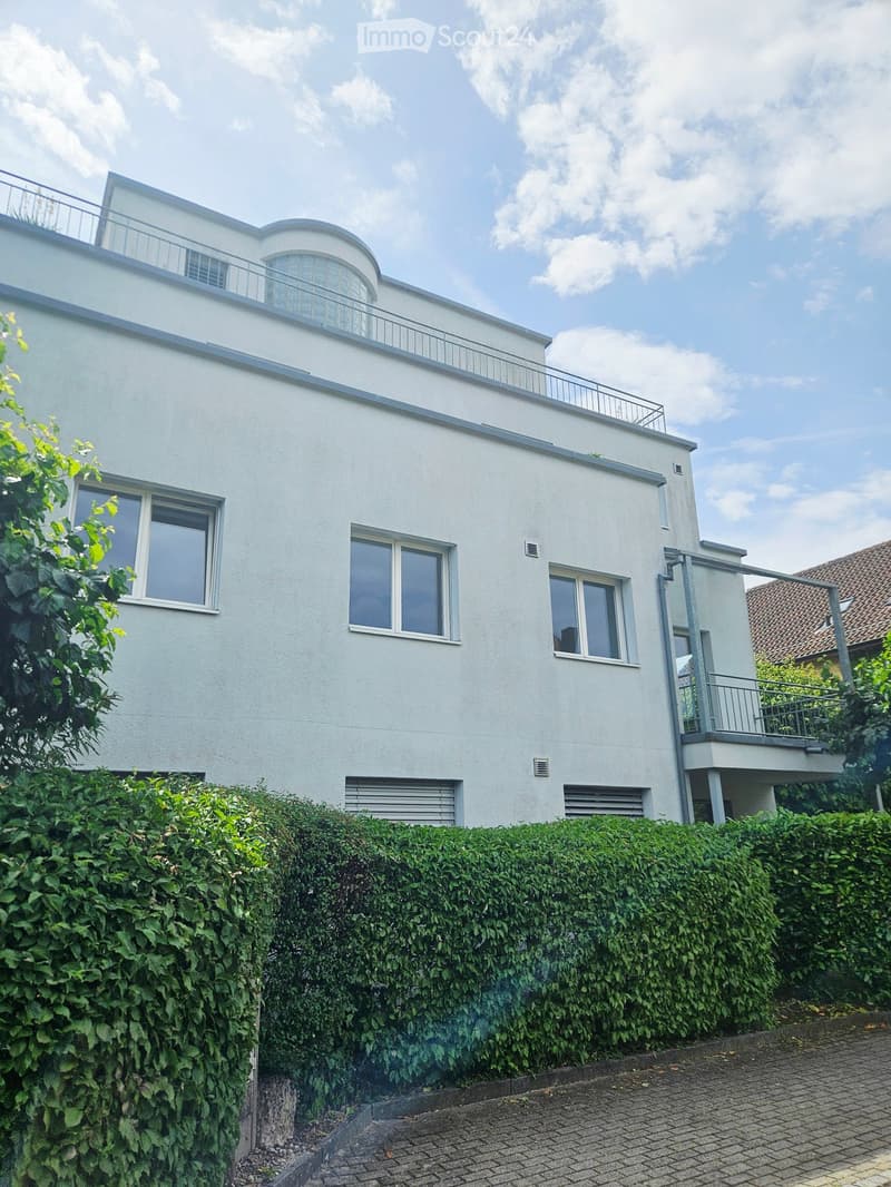 Modern two-story house with white exterior, large windows, and a balcony on the upper level.