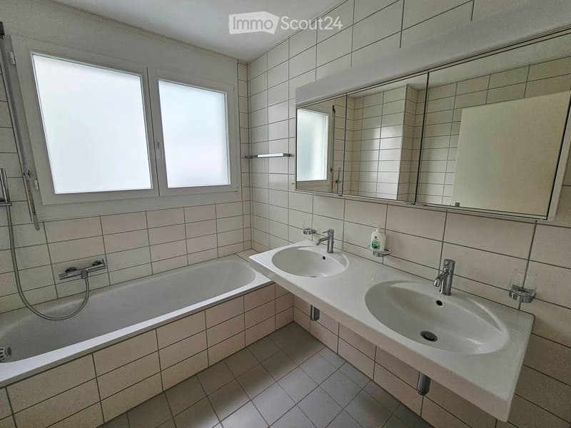 Modern bathroom with a bathtub, double sink, mirror, and tiled walls and floor.